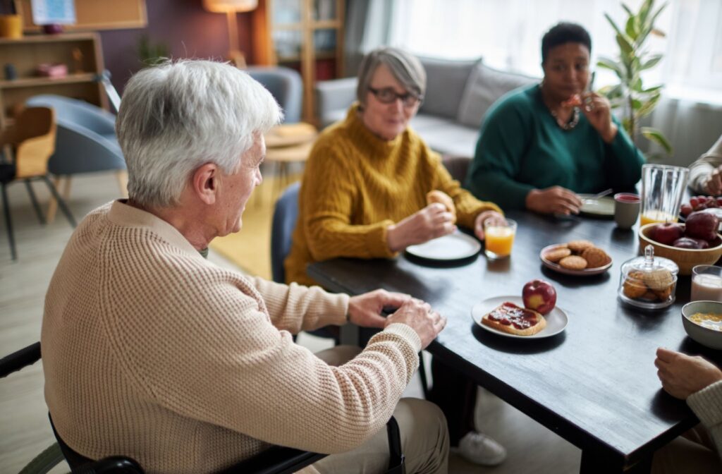 5 seniors sit around a table eating continental breakfast items together.