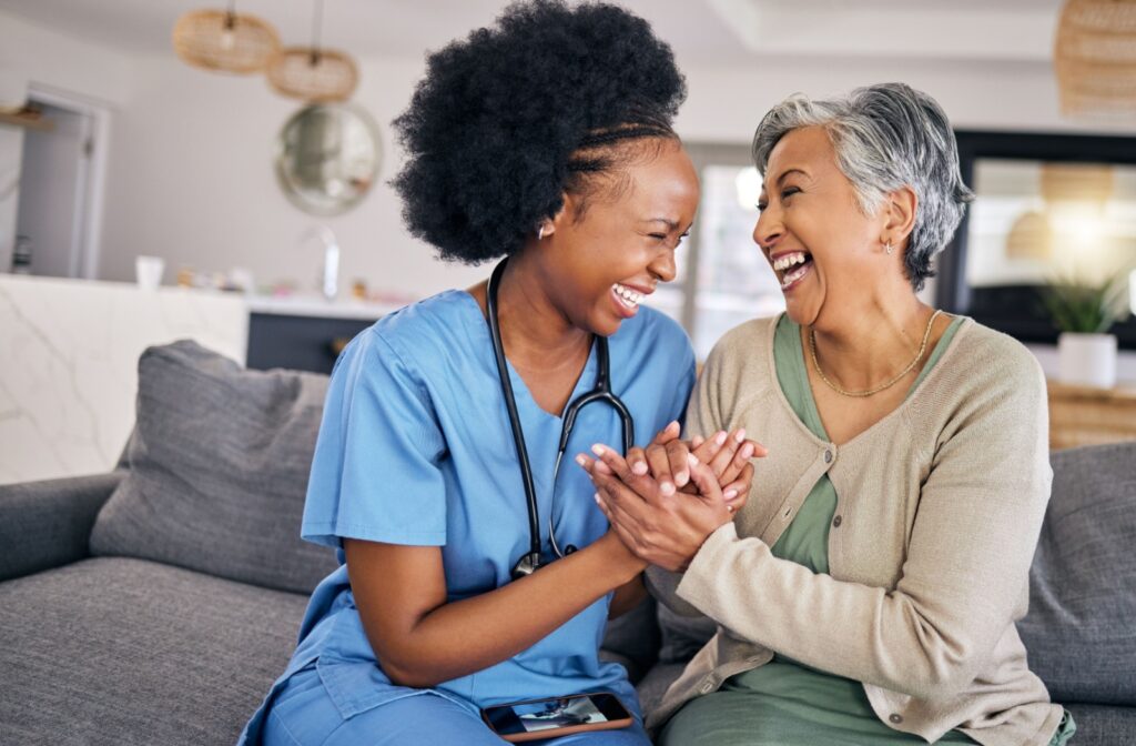 A young caregiver and an assisted living resident clasp hands and laugh together.