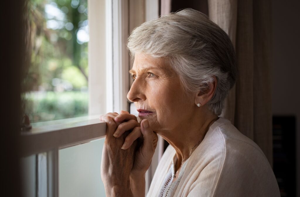 A senior woman with dementia leans against a window