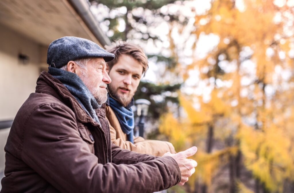 An older adult father standing outside chatting with his adult son about moving into a senior community.