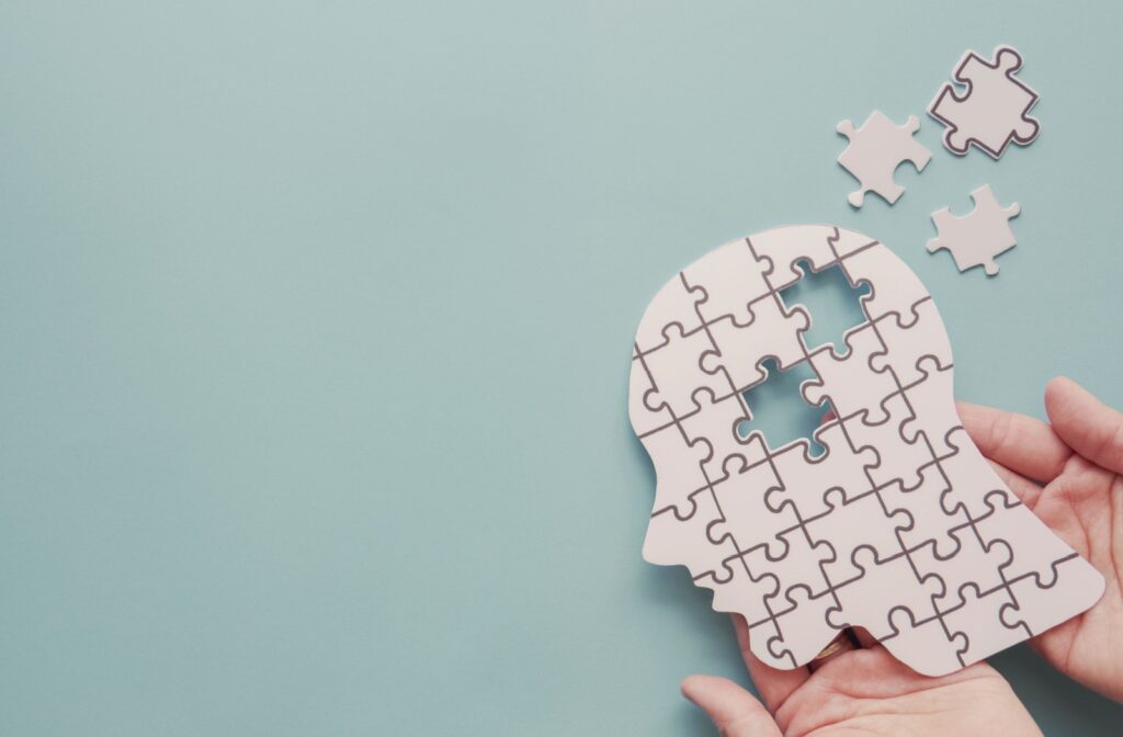 Hands holding a jigsaw puzzle of a person's face with two pieces missing, symbolizing cognitive decline.