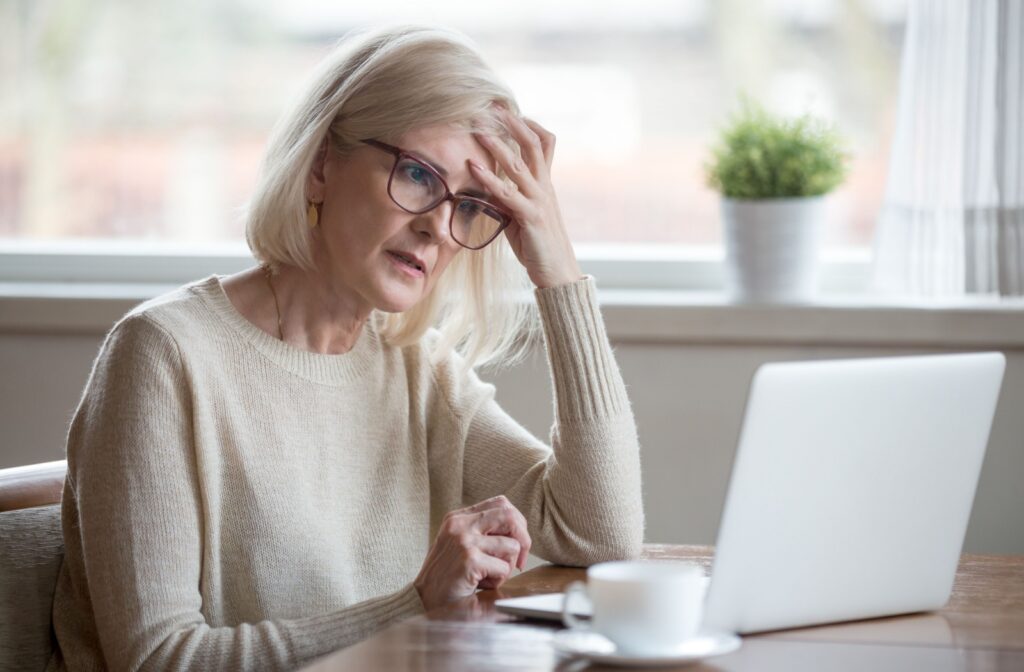 An older adult touches their forehead in confusion while reading something on their computer