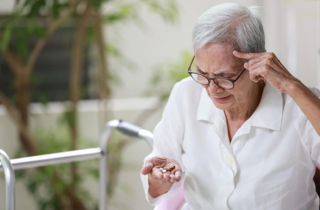 An older adult rubs their forehead while checking their medication, wondering if they've already taken their dose
